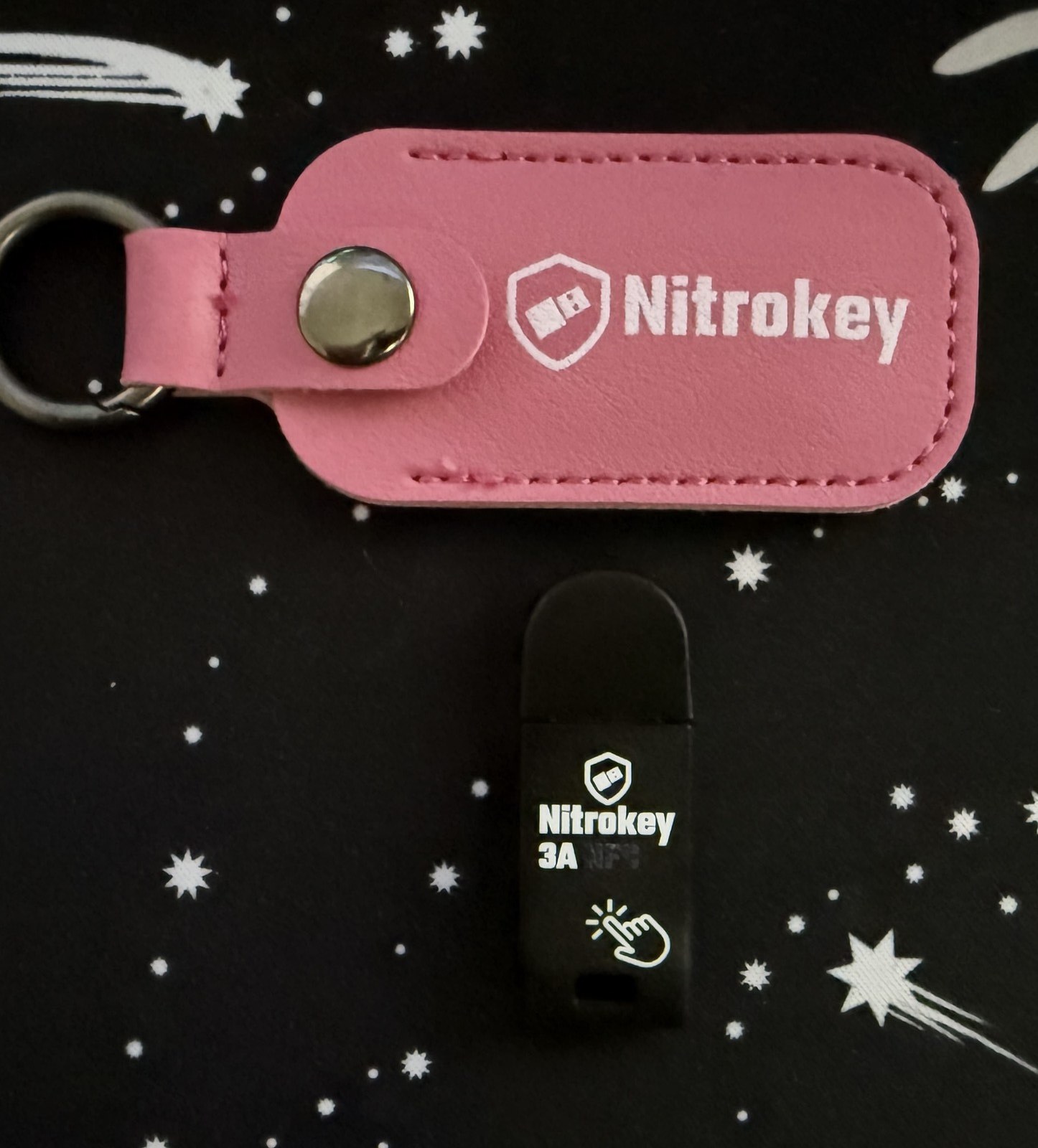 Nitrokey 3A next to the included pink leather pouch with Nitrokey logo