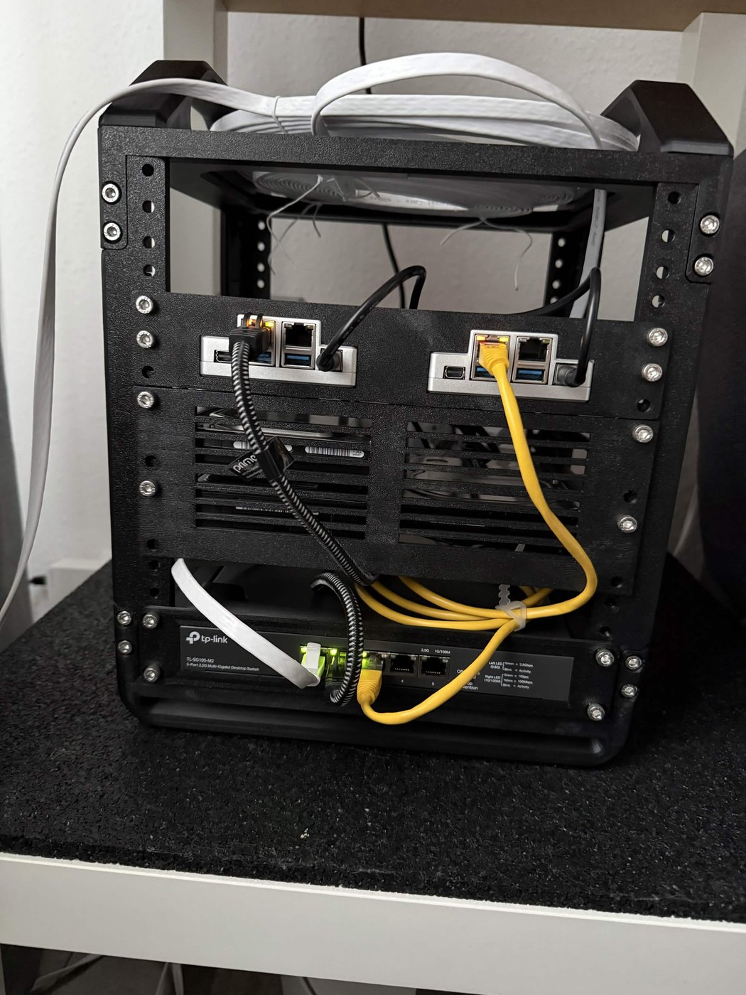 3D-printed 10-inch rack: a TP-Link TL-SG105-M2 switch at the bottom, drives in the middle, two ZimaBoards on top, wired with yellow and white patch cables